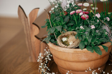 Stylish easter eggs with feather in nest, potted spring flowers  and bunny figurines composition on...
