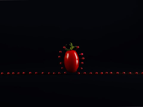 A plum tomato surrounded by red pins against a black background