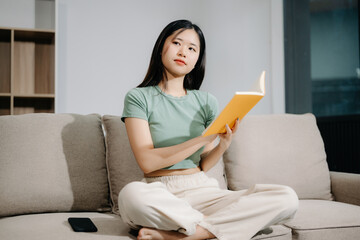 Young Asian woman listening music from headphones and writing note for her work idea in diary book.