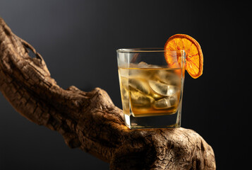 Old fashioned cocktail with ice and dried orange slice on a old snag.