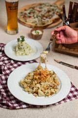 A person's hand uses a fork to take a paste with melted cheese