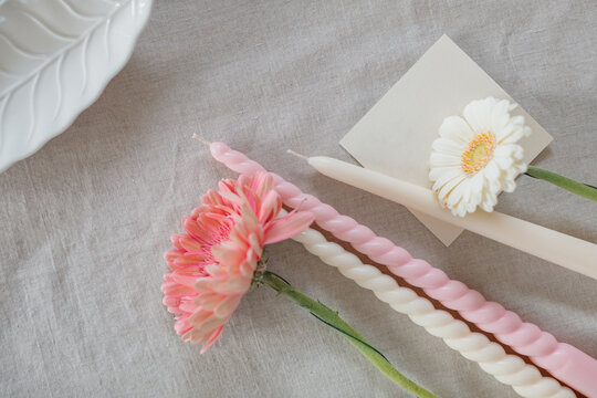 Overhead view of assorted candles, blank paper card and gerbera flowers on a table