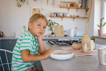 Beautiful blond child, boy, refusing to eat cereal for breakfast at home in the morning