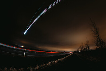 Long exposure of a car passing by and a plane flying over the road at night