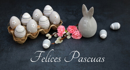 Tarjeta de felicitación Felices Pascuas: Decoración de Pascua con huevos y conejitos de Pascua sobre un fondo de pizarra oscura.