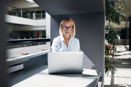 Concentrated busineswoman working online in an office pod on her laptop in a modern office
