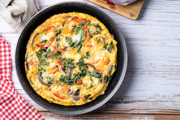 Italian Frittata made with spinach, tomatoes, onion and peppers on white wooden table. Top view. Copy space