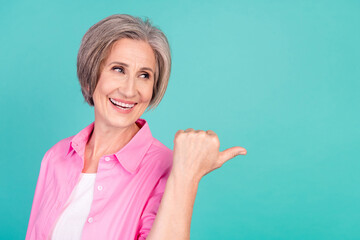 Photo of cheerful mature aged white hair business woman direct thumb empty space curious discounts isolated on cyan color background