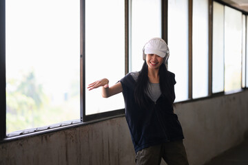 Smiling female hip hop dancer in headphone dancing in an abandoned building on sunny day