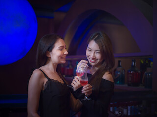 Female friends talking and holding glasses during night party at night club .