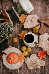 Big mug of hot dark coffee, sweet candies, autumn leaves and handmade woolen clothes on wooden background, vintage scene