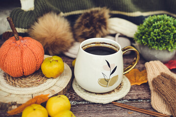 Big mug of hot dark coffee, sweet candies, autumn leaves and handmade woolen clothes on wooden background, vintage scene