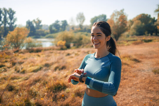 A happy young athletic woman checking her smart watch and looking away after her jogging session in nature