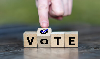 Hand turns wooden cube and puts a tick on the word vote. Symbol for participating in a voting...