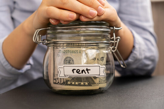 Female hands holding Glass jar full of American currency dollars cash banknote with text RENT. Preparation saving money. Moderate consumption and economy. Collecting money