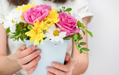 woman holds in her hands a flower arrangement of roses, daisies and chrysanthemums