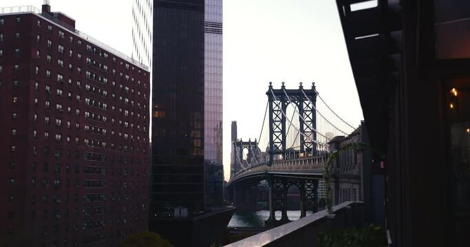 Cinematic shot of majestic Manhattan Bridge surrounded by urban New York buildings in before sunrise glow.