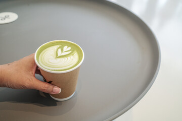 Hand holding matcha latte on a table at cafe