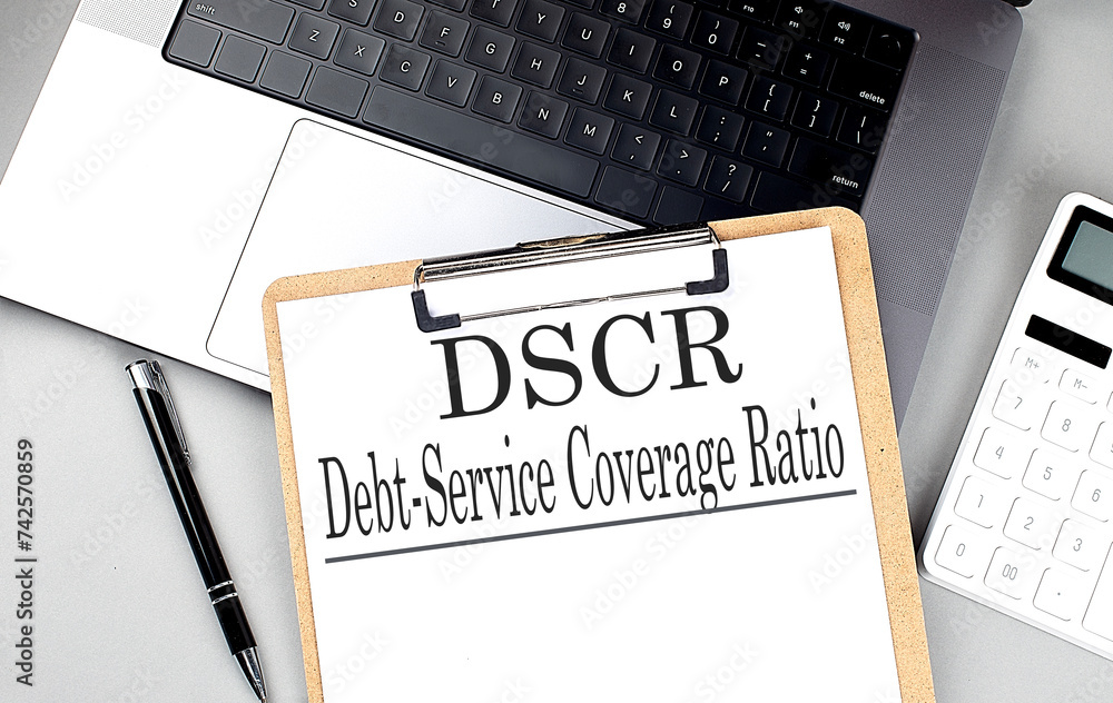 Poster paper clipboard with dscr debt service coverage ratio on laptop with pen and calculator