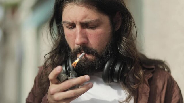Stylish bearded man with long hair, lights a cigarette, confidence, brutality, smoking, attractiveness, zippo, daring, bad guy, openness, people, bad habits, cigarette, smoke, close portrait of a man