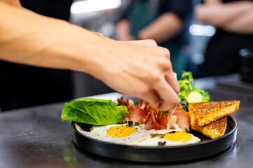 woman chef hand cooking fried eggs with ham, salad and hummus