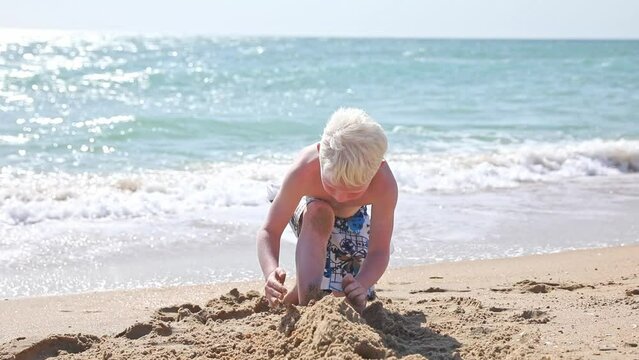 Cute white little boy play with sand on summer tropical beach. Vacation concept. Happy family and childhood