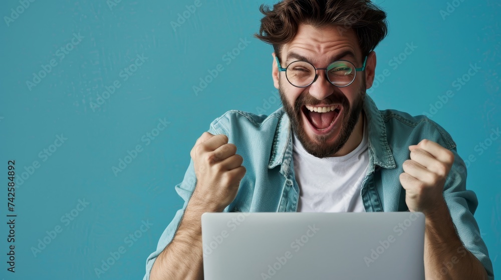 Poster An enthusiastic millennial guy uses a laptop computer for online work or communication on a blue studio background