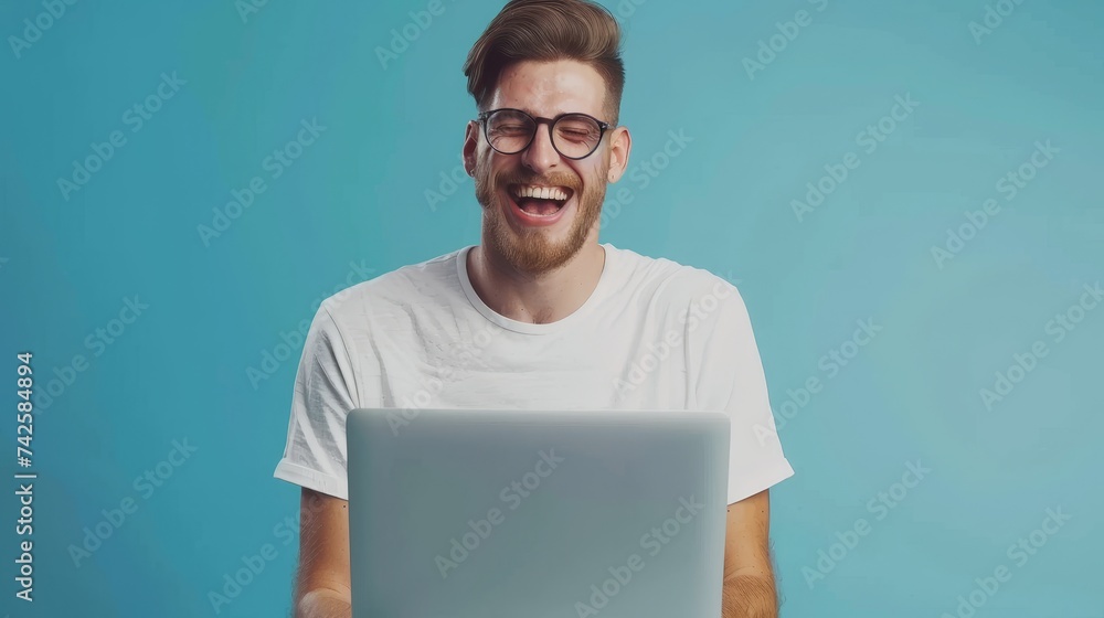 Poster A cheerful millennial man in glasses is using his laptop computer for online work or communication in a blue studio background