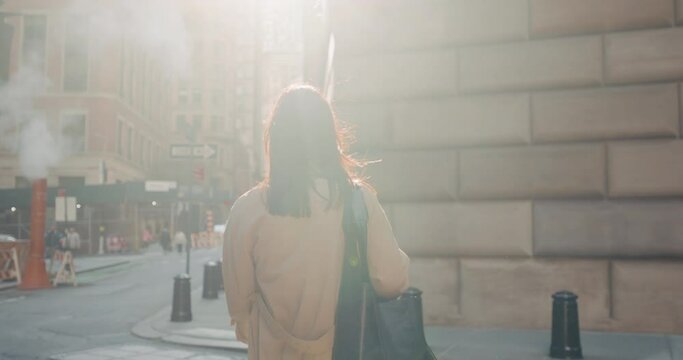 Rear view of a brunette walking the streets of urban New York City, blinded by intense rays of sunlight. Slow motion.