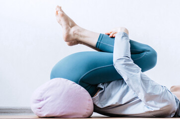 Woman doing yin yoga passive hip stretch exercises on bolster