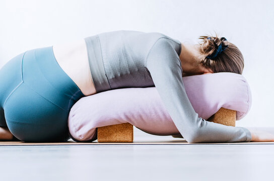 Woman doing restorative yoga twist with bolster on cork blocks