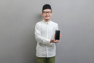 Portrait of an Asian Muslim man wearing a koko shirt and peci with shades of the fasting month,...