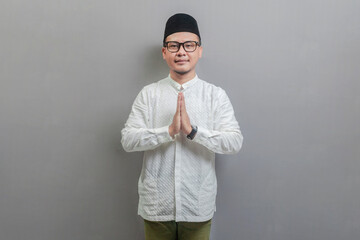 Asian Muslim man wearing a koko shirt and peci with shades of the fasting month, standing with Eid...