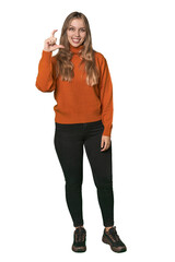 Studio portrait of a blonde Caucasian woman holding something little with forefingers, smiling and confident.