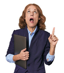 Mid-aged Caucasian with laptop in studio pointing upside with opened mouth.