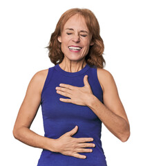 Redhead mid-aged Caucasian woman in studio laughs happily and has fun keeping hands on stomach.