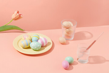 Easter eggs colorful decorated on yellow dish with flower and water cups on a pastel pink background. Eggs symbolize fertility on Easter. Special handmade gifts