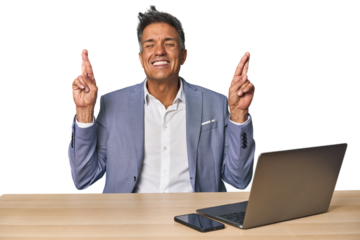 Elegant businessman at desk with laptop crossing fingers for having luck