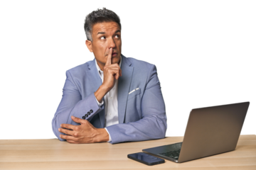 Elegant businessman at desk with laptop looking sideways with doubtful and skeptical expression.