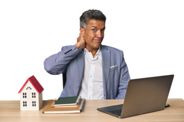 Middle-aged Hispanic businessman with real estate theme touching back of head, thinking and making a choice.