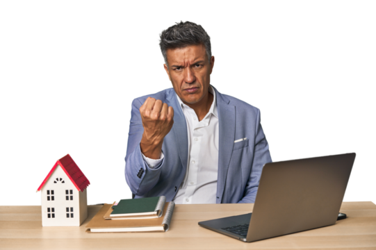 Middle-aged Hispanic businessman with real estate theme showing fist to camera, aggressive facial expression.