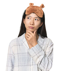 Young Chinese woman in pajamas, mask looking sideways with doubtful and skeptical expression.