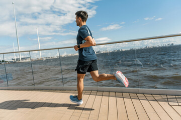 Dynamic young man running along a waterfront with a cityscape in the background.
