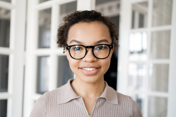 Smiling young professional woman with glasses, standing confidently in a modern office.