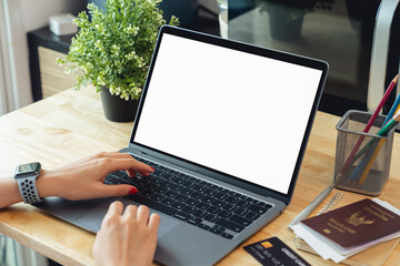 Woman hand using laptop and typing on keyboard with mockup of blank screen on wooden table.