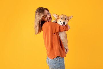 Delighted young woman cradles her beloved corgi dog in her arms, both smiling radiantly, pet...
