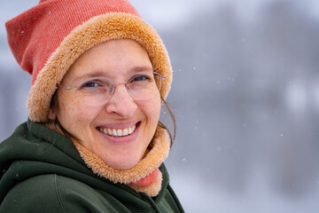 Happy woman in her early 50s outside in cold weather with light snow falling. Plenty of room for copy on right.