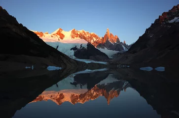 Photo sur Plexiglas Cerro Torre Cerro Torre and Adela Range are reflected in calm waters of Laguna Torre at sunrise, granite mountain peaks and glaciers turning red with rising sun, Southern Patagonian Ice Field in South America