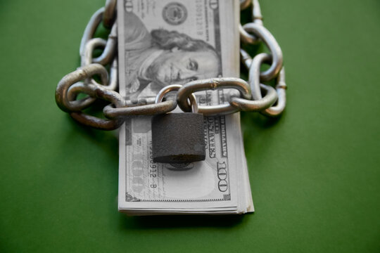A stack of black-and-white hundred-dollar bills and a chain with a lock on the money, financial blocking, account blocking, account arrest, frozen account, financial aid block