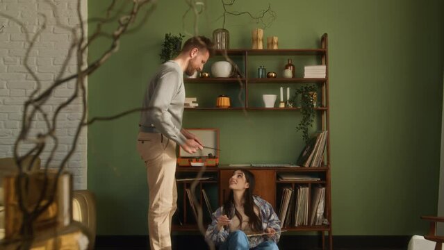 love couple have romantic leisure at home. young man and woman listen music on record player. girl sit on floor and give boyfriend a record